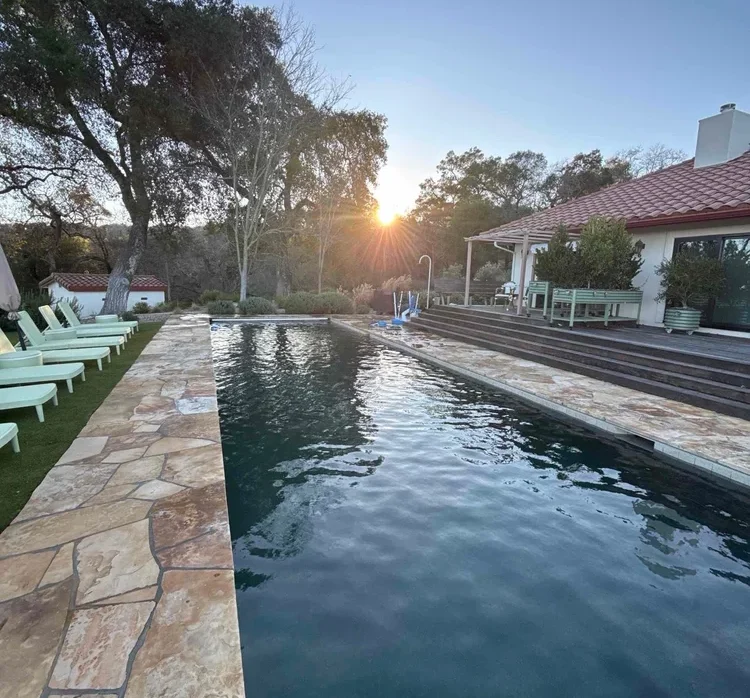 Long rectangular pool at sunset with stone deck and lounge chairs