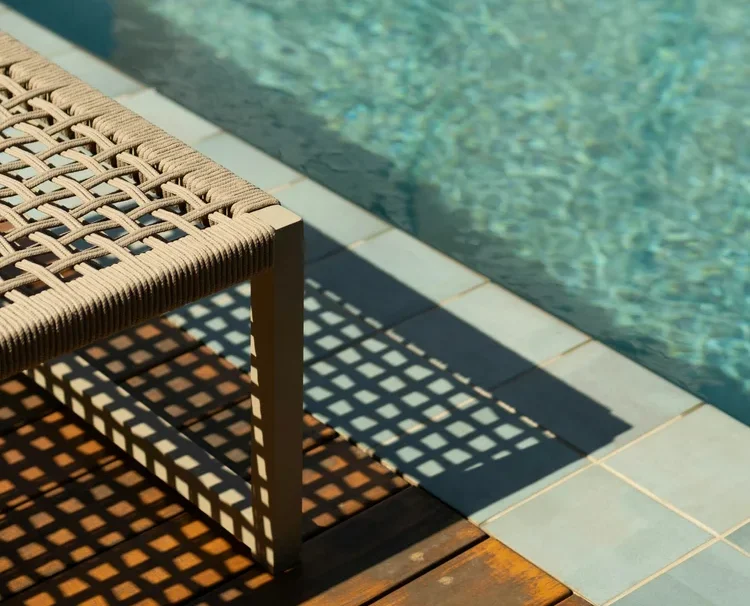 Woven poolside chair casting shadows on the deck