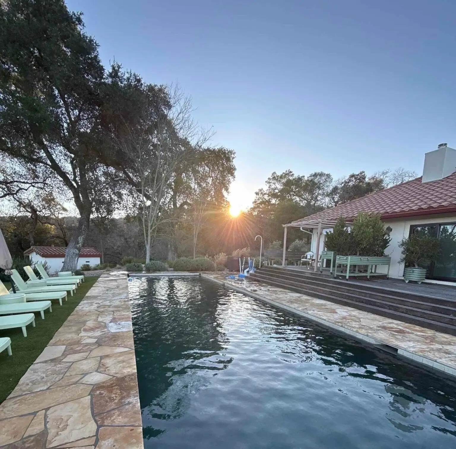 Long rectangular pool at sunset with lounge chairs and stone deck