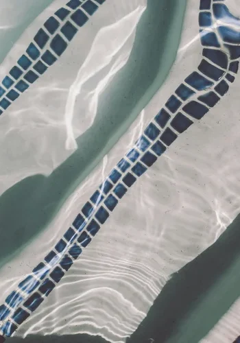 Dark mosaic tile lines on a pool floor under rippling water
