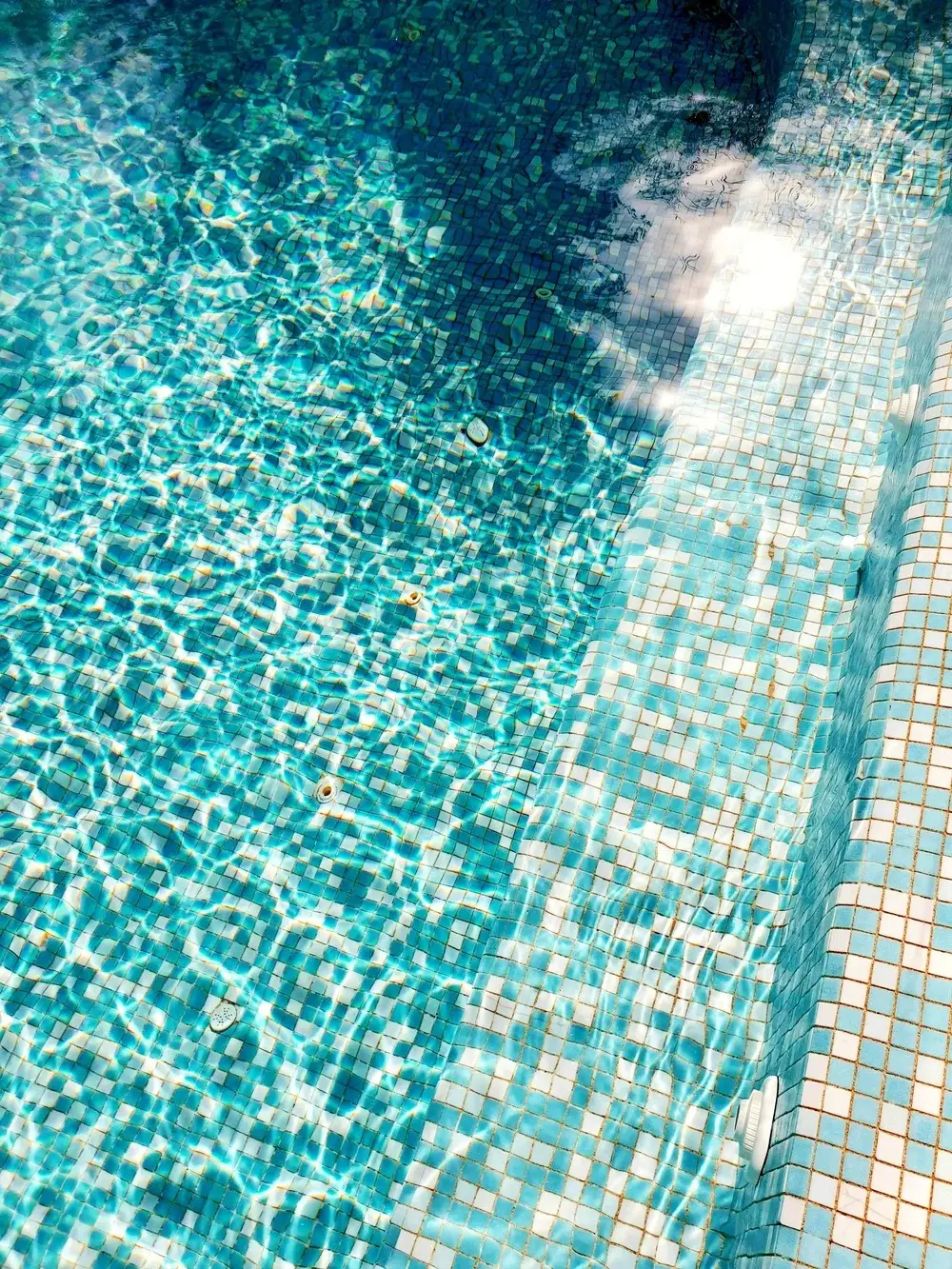 Sunlit clear water over glass pool tile