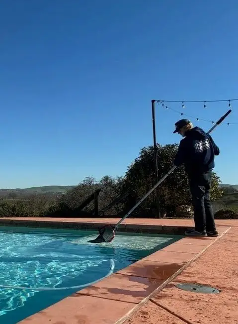 Technician brushing an infinity-edge pool with hillside views