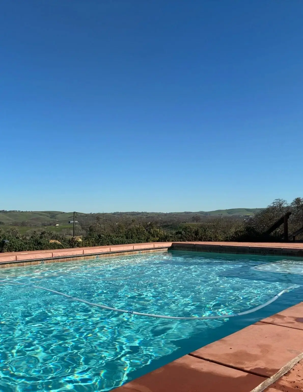 Sparkling backyard pool under blue sky with hillside view