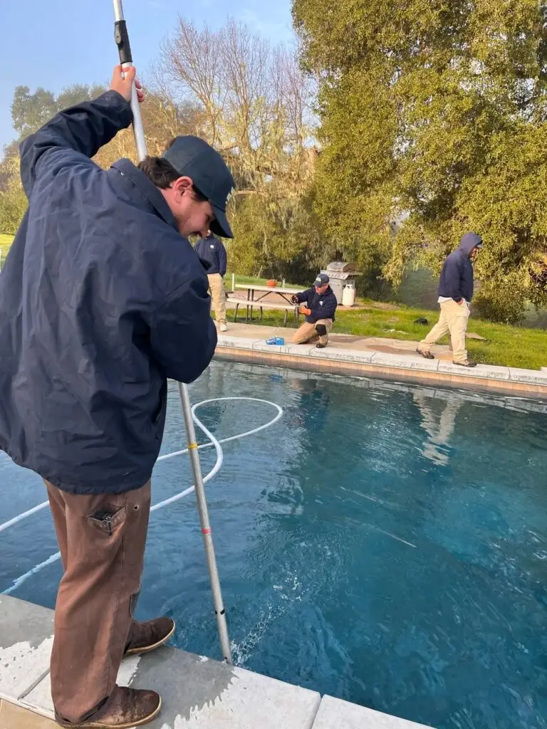 Technician brushing pool walls with a second technician in the background