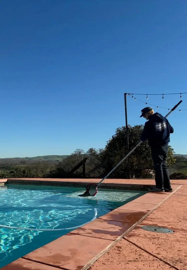Pool technician skimming a backyard pool on a sunny day
