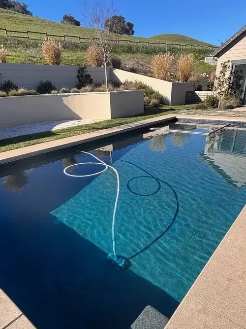 Dark-finish pool with automatic cleaner hose at a hillside home